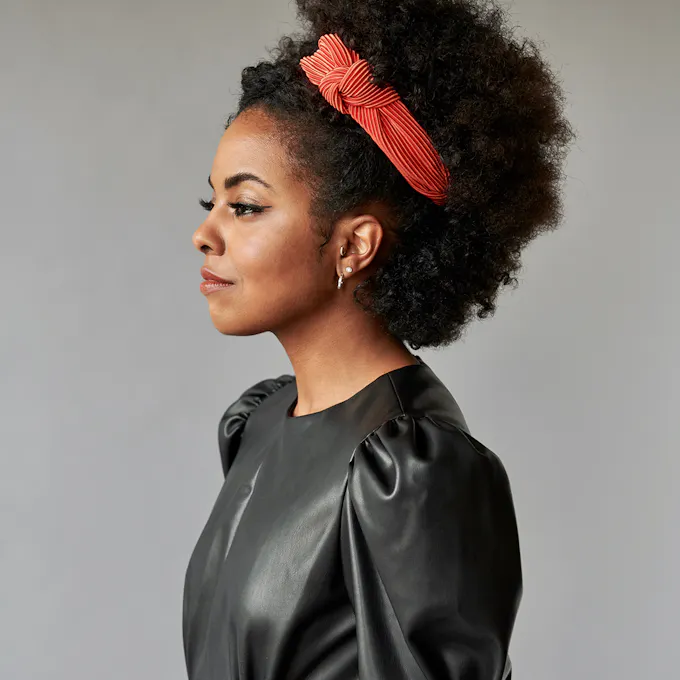 Adrienne Warren stands in profile in a black leather dress