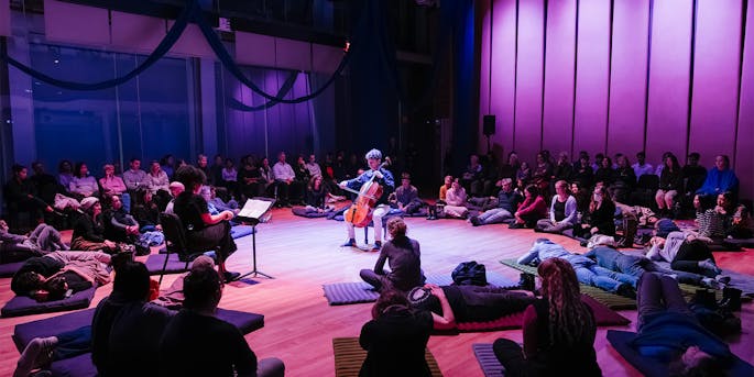 People laying on mats surrounding a cellist