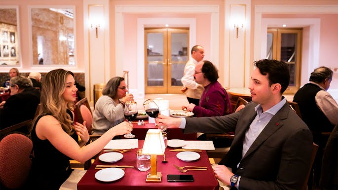 Two people sitting at a table clinking wine glasses together