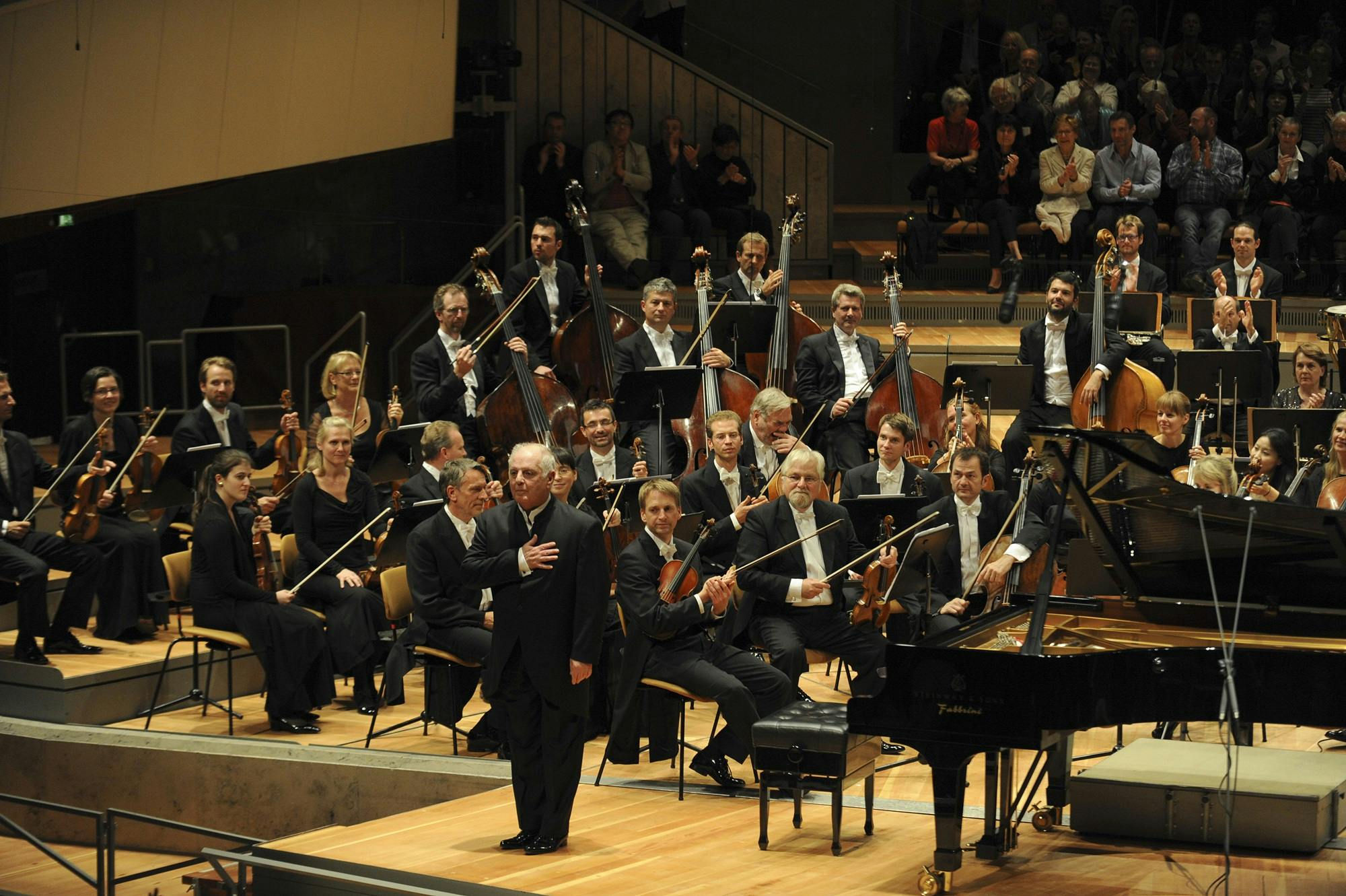 Daniel Barenboim standing on stage for applause, with an orchestra behind