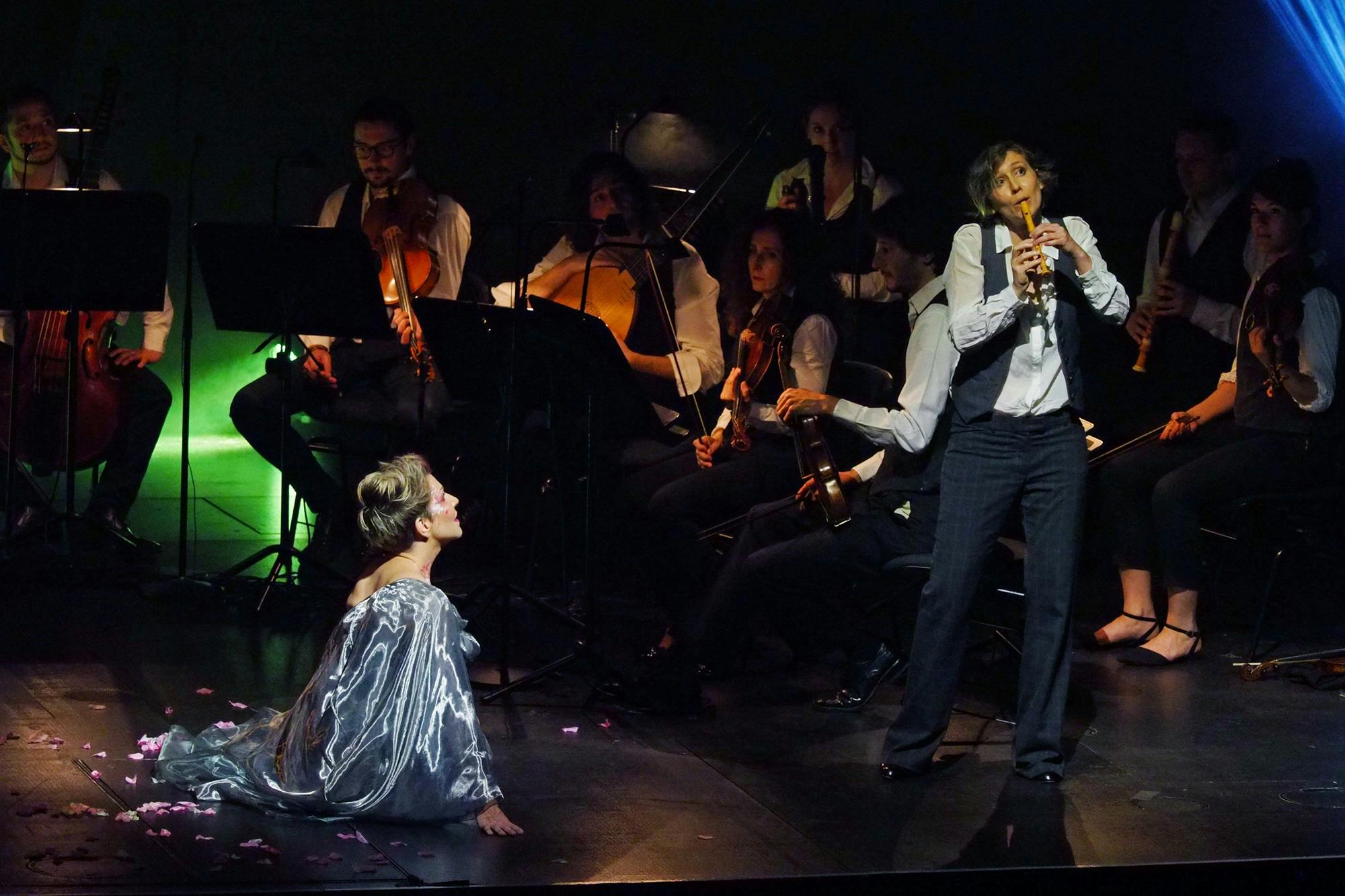 Joyce DiDonato sitting on stage, looking at a performer playing a recorder