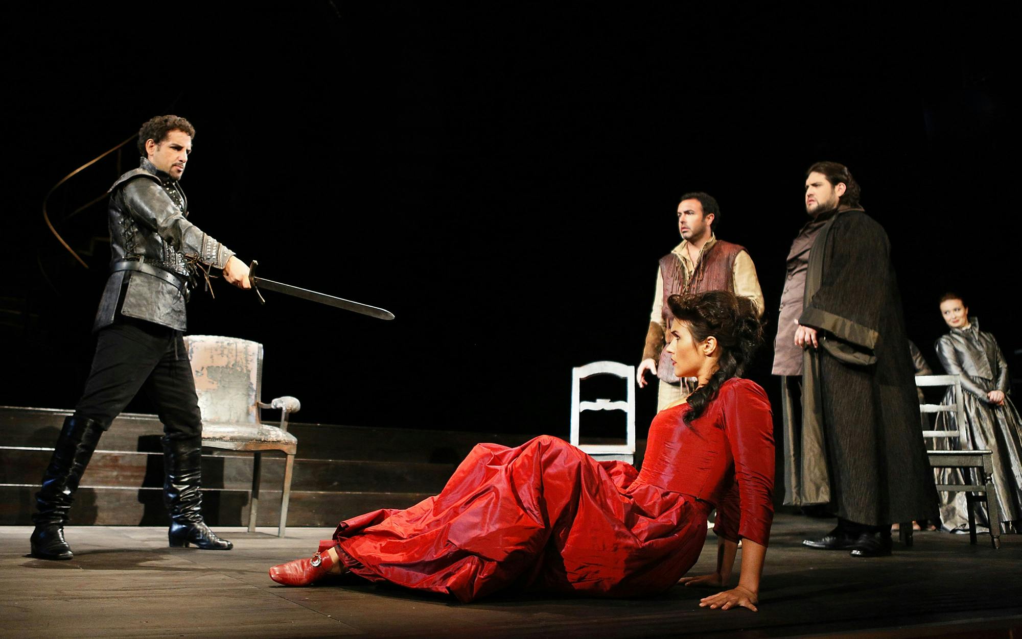 Juan Diego Flórez standing and holding a sword pointed at Olga Peretyatko, with performers standing to the side.