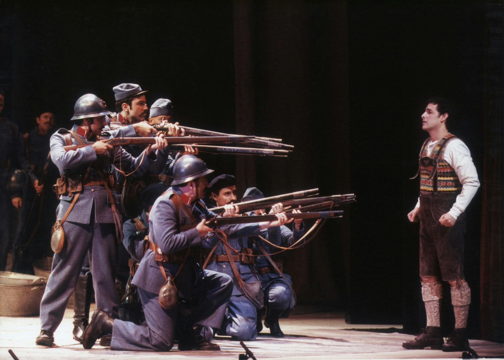 Soldiers standing and kneeling, pointing guns at Juan Diego Flórez.