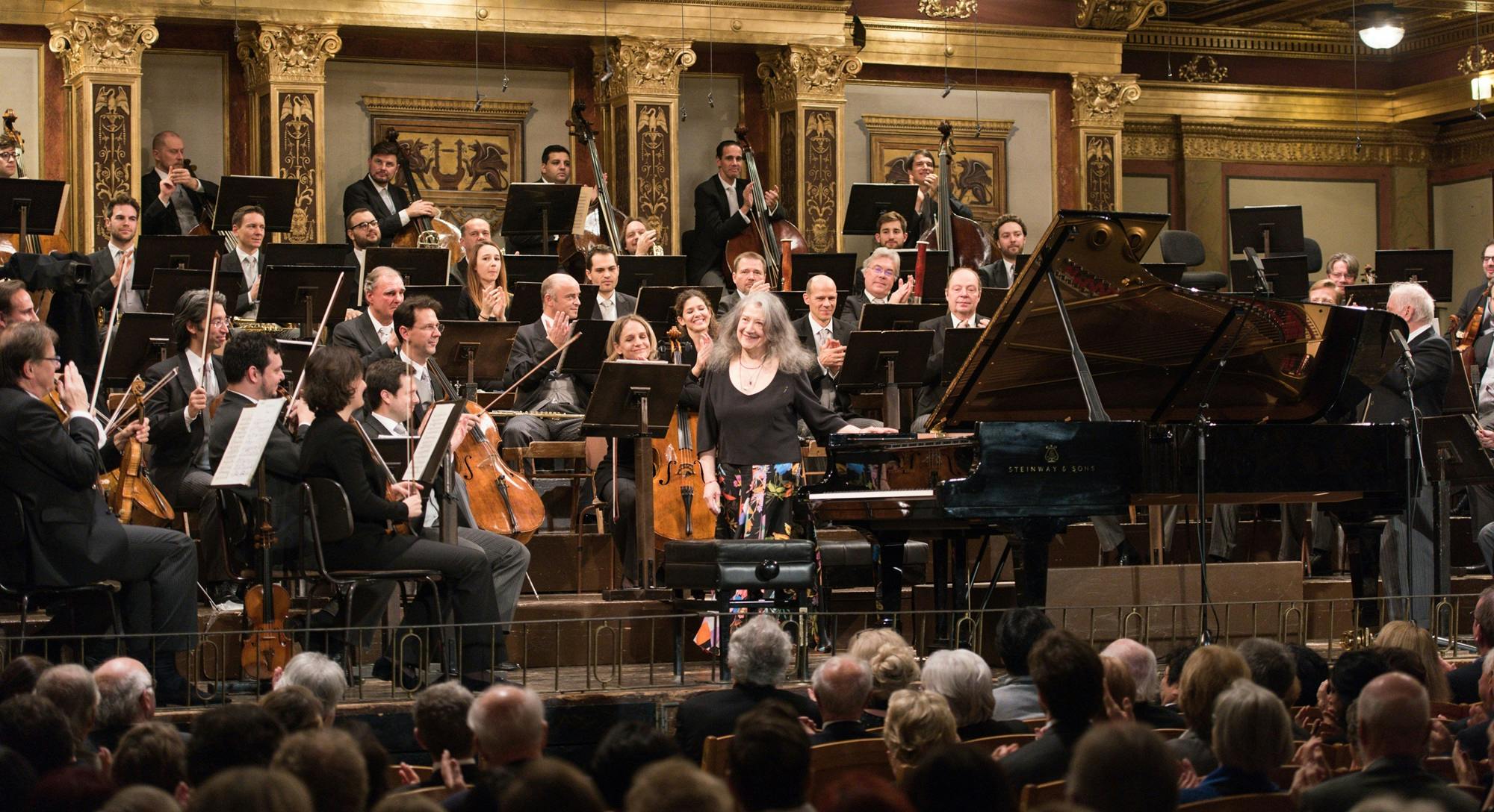 Martha Argerich standing for applause in front of an orchestra.