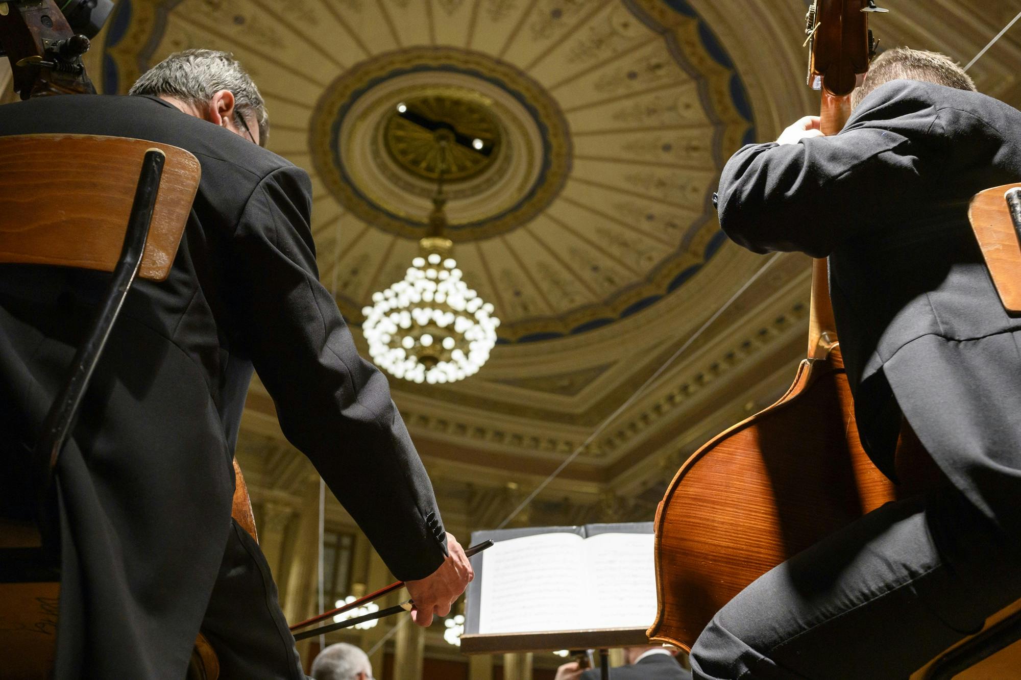 Two cellists playing with the roof of the concert hall visible above them