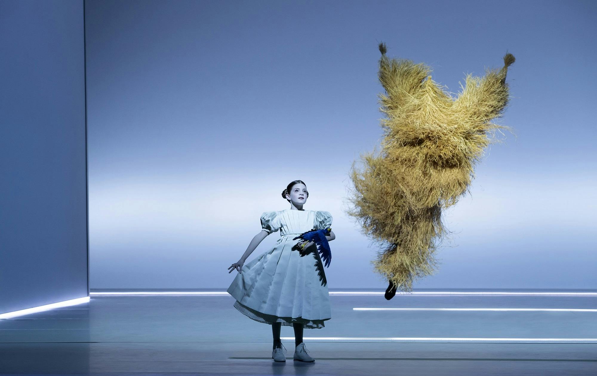 A young actor holding a toy bird, and an actor dressed in a straw costume jumping in the air