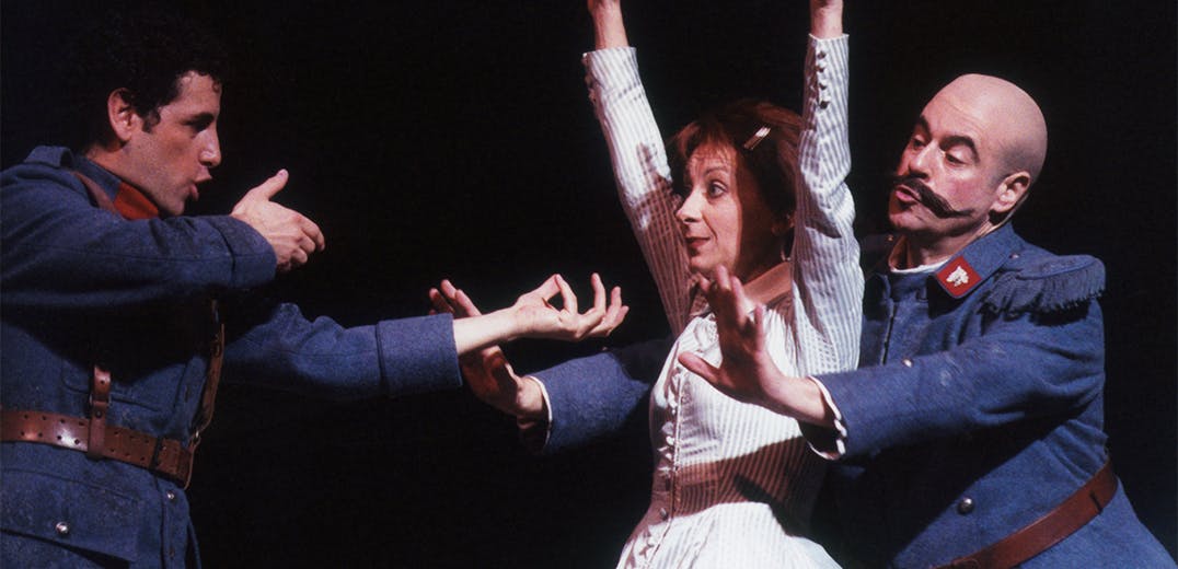 Juan Diego Flórez pointing an imaginary gun at Natalie Dessay, whose hands are raised in the air; a third performer stands behind Dessay with arms pointed out toward Flórez.
