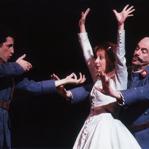 Juan Diego Flórez pointing an imaginary gun at Natalie Dessay, whose hands are raised in the air; a third performer stands behind Dessay with arms pointed out toward Flórez.