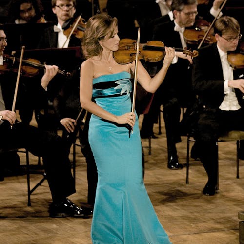Anne-Sophie Mutter playing the violin on stage with an orchestra.