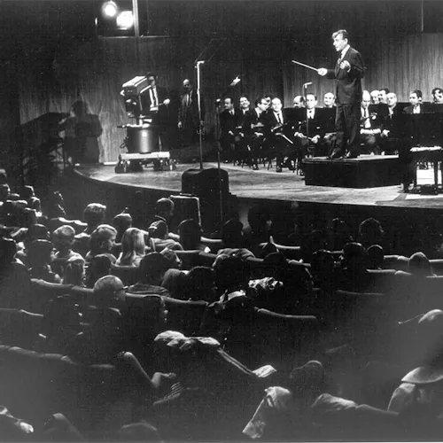 Leonard Bernstein standing on the podium, with an orchestra, facing the audience