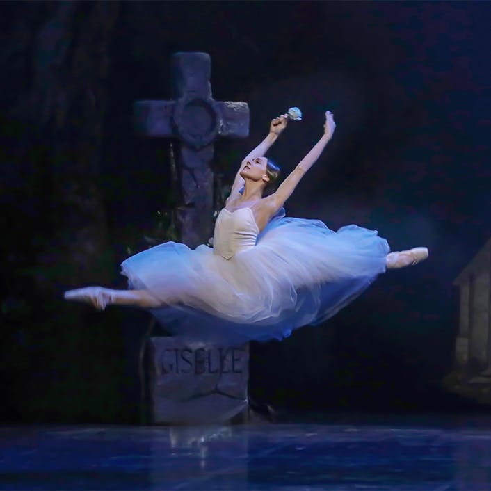 A dancer jumping in the air with legs extended and arms raised in the air