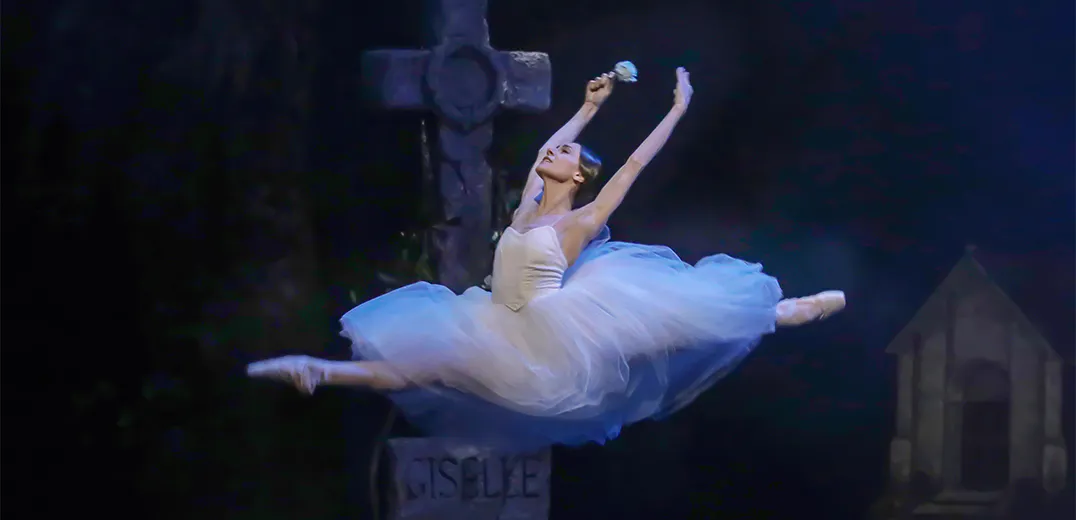 A dancer jumping in the air with legs extended and arms raised in the air
