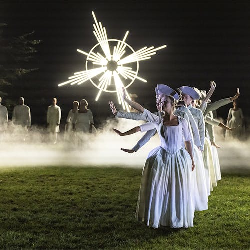 Dancers forming a line on a grass field on a foggy night