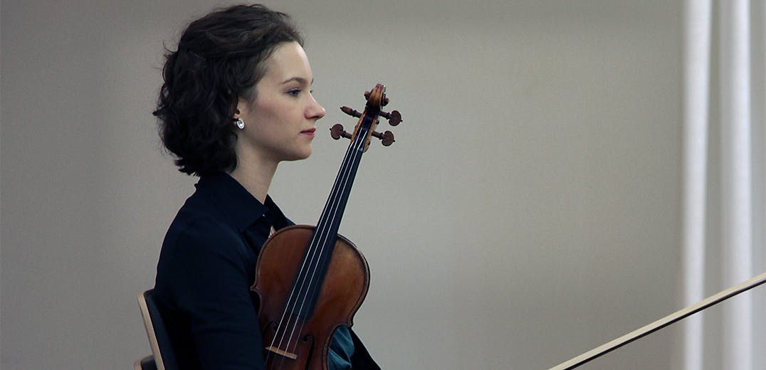 Hilary Hahn sitting and holding a violin.