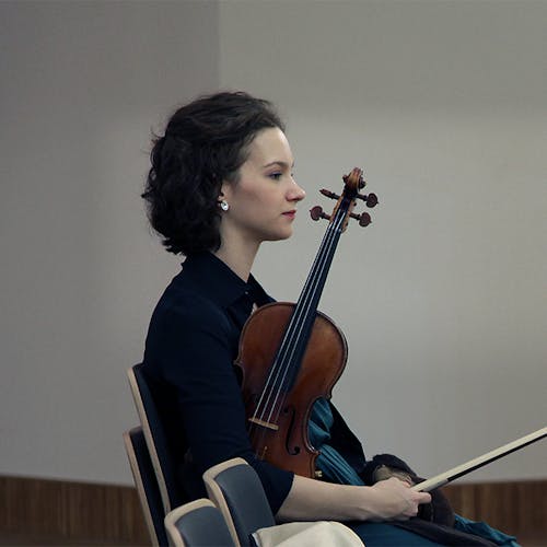 Hilary Hahn sitting and holding a violin.