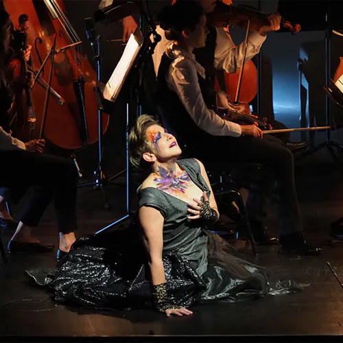 Joyce DiDonato kneeling on the ground in front of string instrumentalists