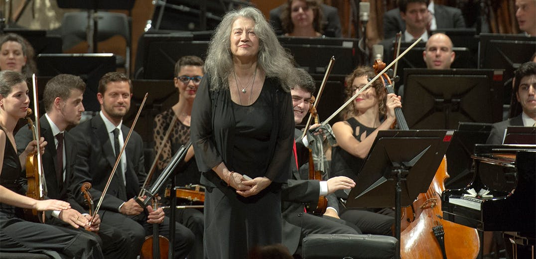 Martha Argerich standing in front of an orchestra for applause