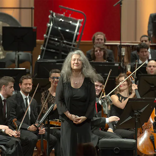 Martha Argerich standing in front of an orchestra for applause