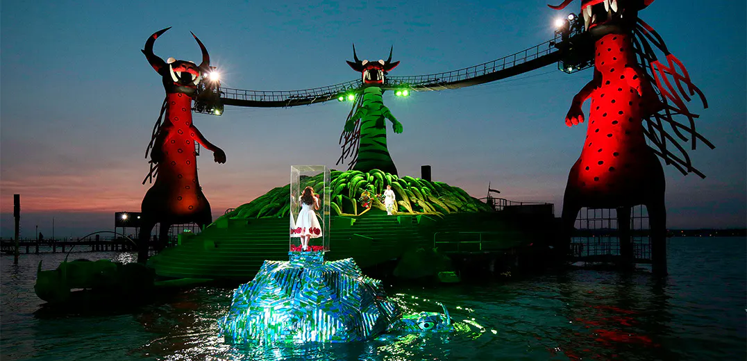 A child standing in a glass box surrounded by a river, looking at bridge held up by three monsters.