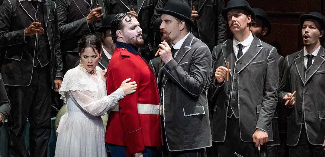 A person in a white dress standing with a person in a red suit, next to three people in grey suits with black bowler hats