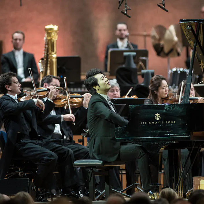 Lang Lang playing the piano with orchestra members