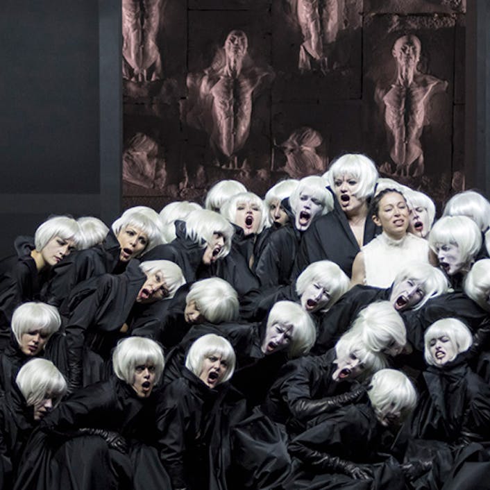 A large group of people with black cloaks and white hair standing in a group, with a person in a white dress and black hair stands in the middle
