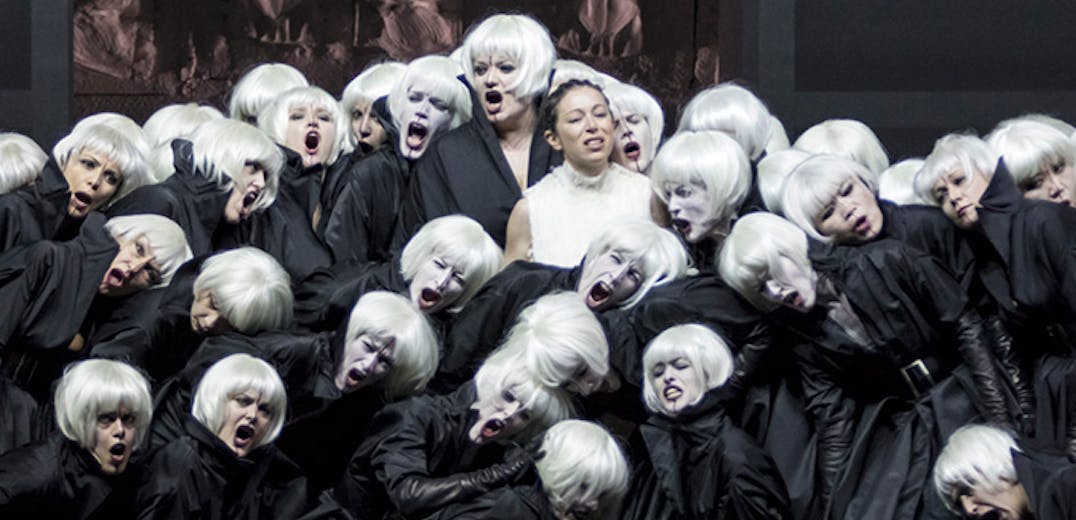 A large group of people with black cloaks and white hair standing in a group, with a person in a white dress and black hair stands in the middle