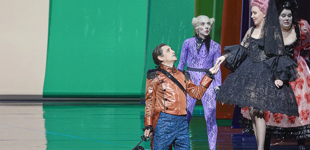 Juan Diego Flórez kneeling on staging, holding hands with a standing performer; two other performers stand around them.