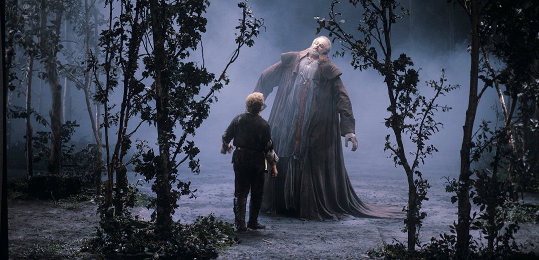 A person in a forest, standing in front of a towering figure