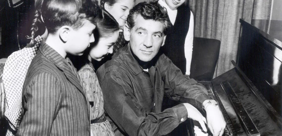 Leonard Bernstein sitting at the piano with a group of children