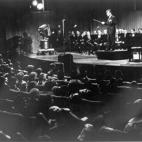 Leonard Bernstein standing on the podium, with an orchestra, facing the audience