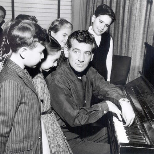 Leonard Bernstein sitting at the piano with a group of children