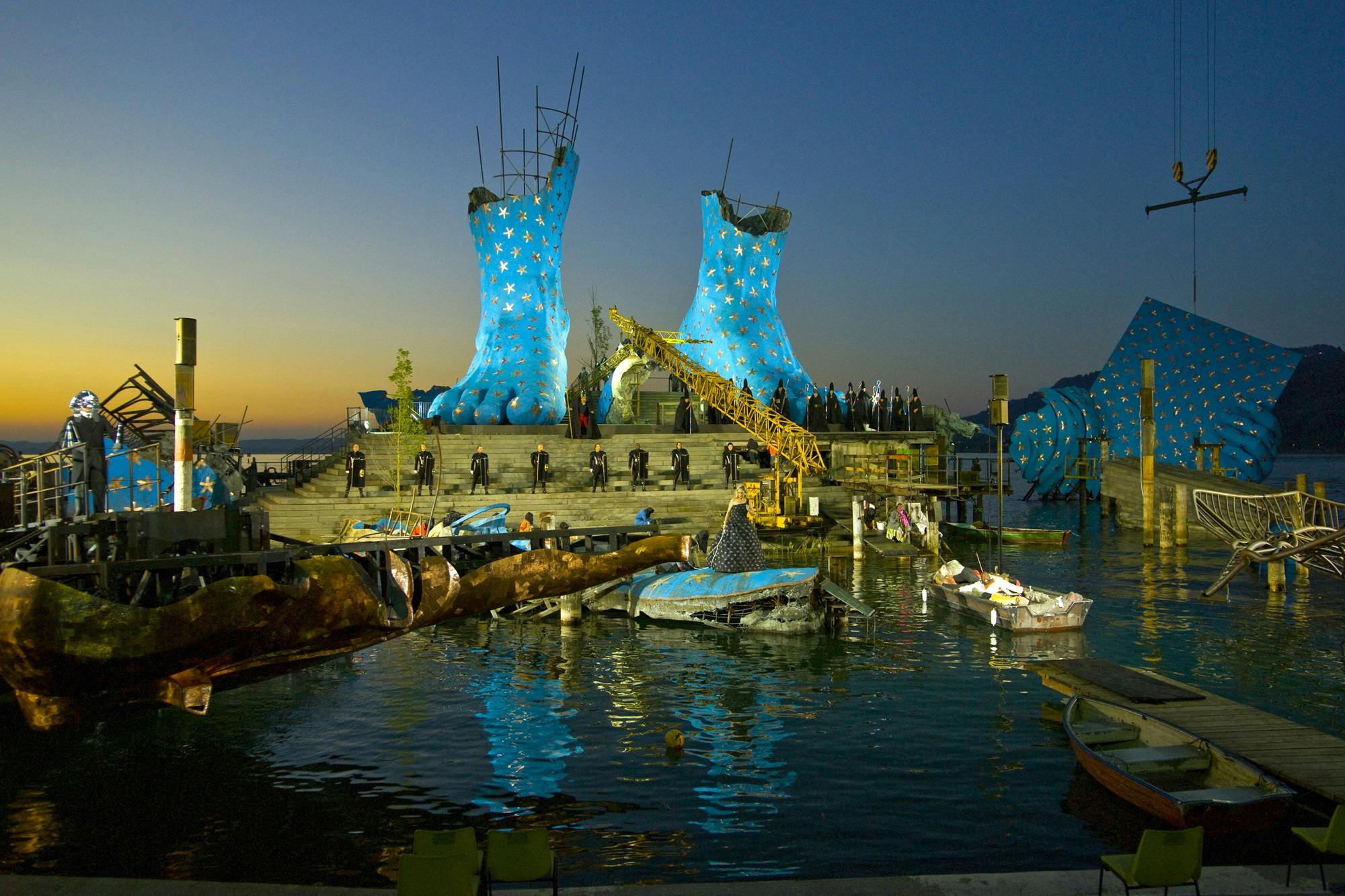 Two feet painted blue with yellow stars placed upon a stage of stone steps, suspended above a body of water