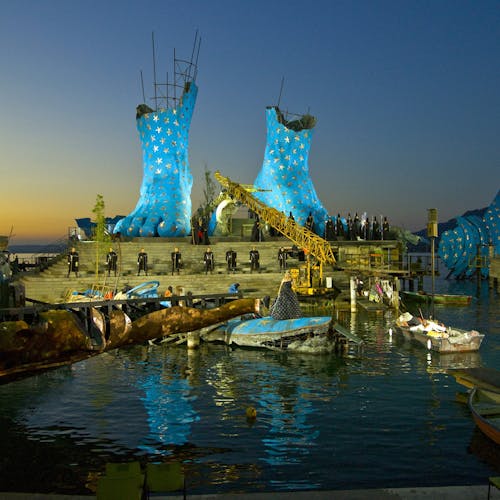 Two feet painted blue with yellow stars placed upon a stage of stone steps, suspended above a body of water